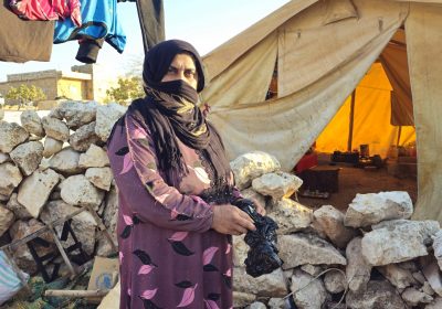 In Photo: Zahra, 40, burning plastic to keep her family warm
 
What does winter feel like in Syria? When temperatures drop to -3 °C outside and inside tents? When families are looking for ways to keep warm? It means collecting wood from trees and bushes that are no longer there, as 14 years of conflict have changed the whole landscape of the country. The area once lush with trees is now only rocks and sand. Shelling has destroyed the land. And people have cut down the remaining trees to keep warm in winter. It means children go out searching for trash: discarded plastic bags and bottles, old shoes and clothing. Anything that can be burnt to keep warm, while the black toxic heavy smoke fills their lungs and tents. It means that when the rain comes, the roofs of the tents collapse, and food storage is destroyed. It means not being able to sleep at night, feeling the pain of cold in their joints. It means taking a spoon to crack the ice of their water barrels inside the tents to get to the drinking water. It means being scared when the wind blows and temperatures drop.
 
Zahra cannot even think about returning home. Her house was damaged heavily. She lives in a tent with her seven children and depends on the only hospital functioning in the area for her sick daughter’s treatment. In winter, Zahra’s children roam the camp and surrounding area looking for anything that might burn. They look for trash such as plastic bags, bottles or old shoes and clothing. “My sick daughter coughs and spits blood whenever I turn on the heater and burn the plastic. It’s the black heavy smoke that harms her. But I need to keep the children warm.” She even cooks over this fire, as she cannot afford fuel for heating. “Sometimes I use straw from livestock. Sometimes I have nylon. We use whatever we can get. We do not have the luxury to choose what to burn.”